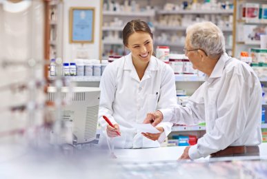 A young pharmacist helping an elderly customer at the prescription counter. 