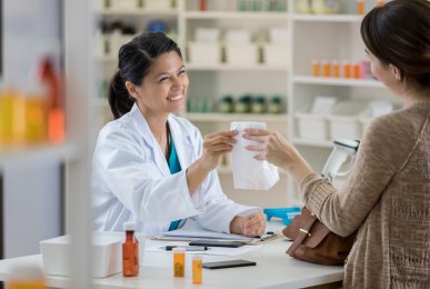 Friendly pharmacist hands a paper bag to young female customer at the checkout counter
