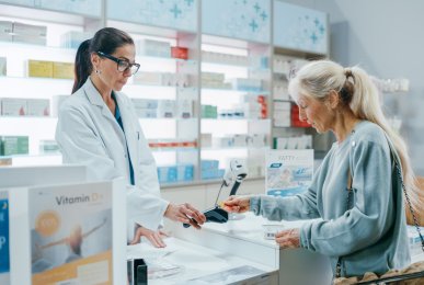 Female pharmacist services senior female customer buying prescription medicine package and paying using contactless method