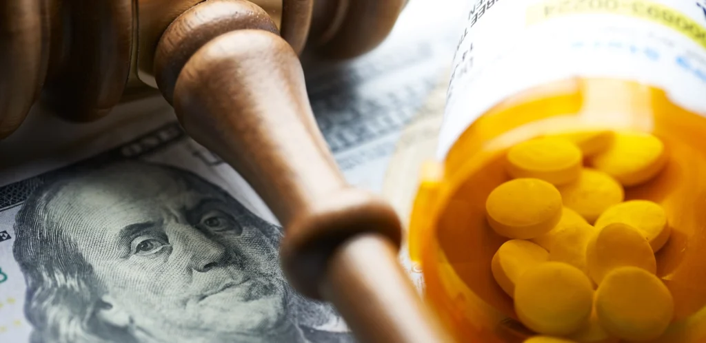 Image of a gavel, a hundred dollar bill, and prescription medication on a table